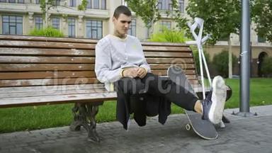年轻人坐在公园的长凳上，一边用<strong>手机</strong>听音乐，然后<strong>拿起</strong>拐杖和滑板